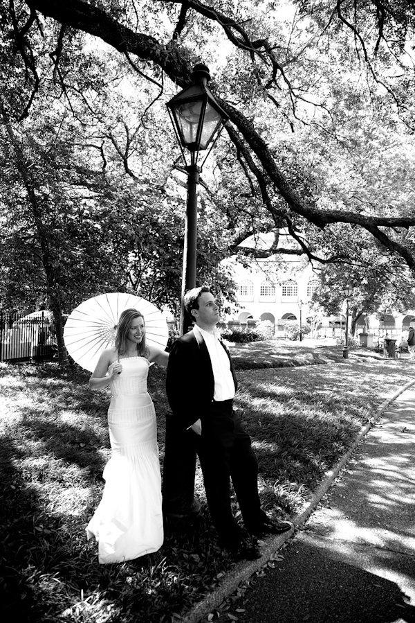 black and white photo of the bride and groom posing under a streetlamp in a park - bride is wearing a sheath style dress holding a parasol - photo by North Carolina based wedding photographers Cunningham Photo Artists